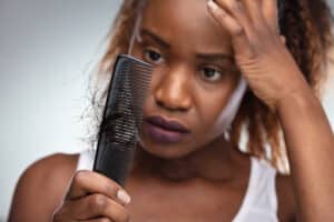 A woman with hair disease looking at a comb with strands of hair stuck in it